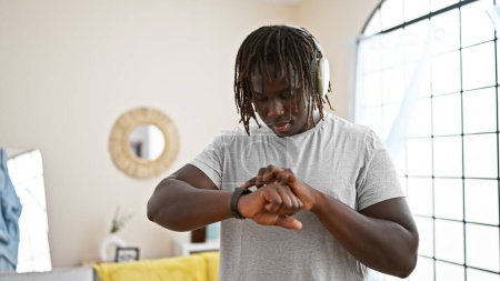 Foto de Hombre afroamericano escuchando música mirando reloj en casa - Imagen libre de derechos