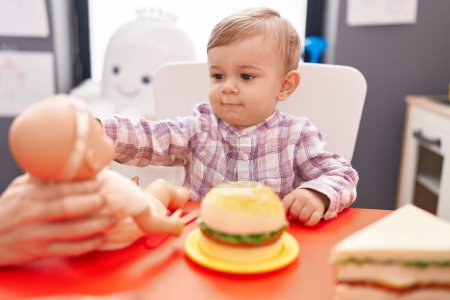 Foto de Adorable chico caucásico jugando con muñeca y juguete de comida en el jardín de infantes - Imagen libre de derechos