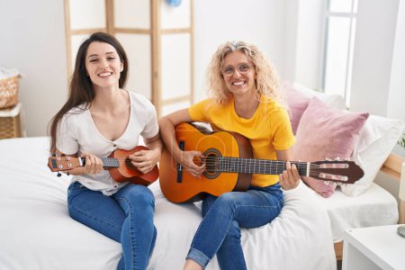 Photo for Two women mother and daughter playing classical guitar and ukulele at bedroom - Royalty Free Image