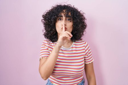 Foto de Joven mujer de Oriente Medio de pie sobre fondo rosa pidiendo estar tranquilo con el dedo en los labios. silencio y concepto secreto. - Imagen libre de derechos