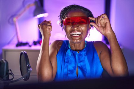 Téléchargez les photos : Femme africaine avec dreadlocks jouer à des jeux vidéo portant des lunettes de réalité virtuelle criant fier, célébrant la victoire et le succès très excité avec bras levé - en image libre de droit