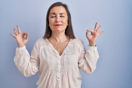 Téléchargez les photos : Femme hispanique du Moyen Âge debout sur fond bleu détendu et souriant avec les yeux fermés faisant geste de méditation avec les doigts. concept de yoga. - en image libre de droit