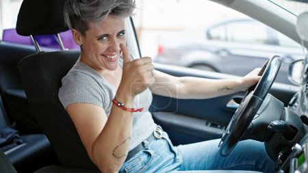 Photo for Young woman driving car doing thumb up gesture at street - Royalty Free Image