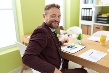 Téléchargez les photos : Homme d'âge moyen travailleur d'affaires souriant confiant assis sur la table au bureau - en image libre de droit