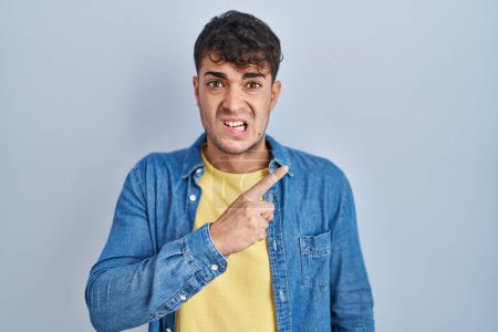 Téléchargez les photos : Young hispanic man standing over blue background pointing aside worried and nervous with forefinger, concerned and surprised expression - en image libre de droit