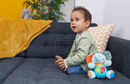 Photo for Adorable hispanic boy sitting on sofa playing with elephant toy at home - Royalty Free Image
