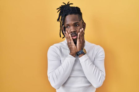 Photo for African man with dreadlocks wearing turtleneck sweater over yellow background tired hands covering face, depression and sadness, upset and irritated for problem - Royalty Free Image