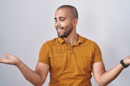 Foto de Hombre hispano con barba de pie sobre fondo blanco sonriendo mostrando ambas manos palmas abiertas, presentando y comparando publicidad y equilibrio - Imagen libre de derechos