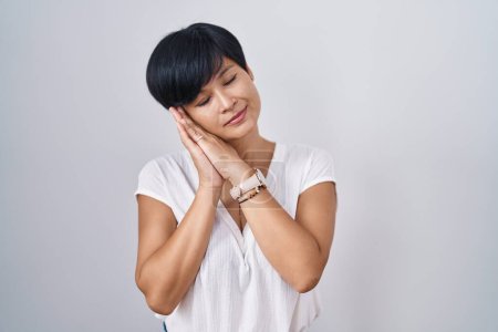 Photo for Young asian woman with short hair standing over isolated background sleeping tired dreaming and posing with hands together while smiling with closed eyes. - Royalty Free Image
