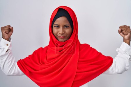 Photo for Young arab woman wearing traditional islamic hijab scarf showing arms muscles smiling proud. fitness concept. - Royalty Free Image