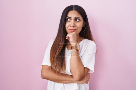 Téléchargez les photos : Jeune femme arabe debout sur fond rose pensant inquiet d'une question, préoccupé et nerveux avec la main sur le menton - en image libre de droit