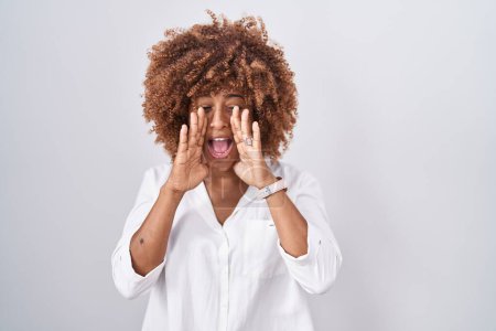 Photo for Young hispanic woman with curly hair standing over white background shouting angry out loud with hands over mouth - Royalty Free Image