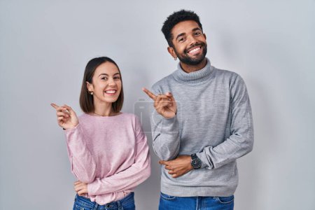 Photo for Young hispanic couple standing together with a big smile on face, pointing with hand finger to the side looking at the camera. - Royalty Free Image