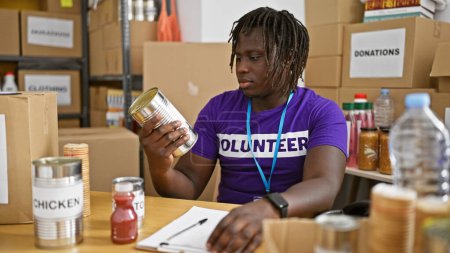 Téléchargez les photos : Un volontaire afro-américain tenant de la nourriture en conserve au centre caritatif - en image libre de droit