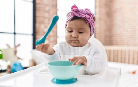 Photo for Adorable hispanic baby holding spoon sitting on highchair at bedroom - Royalty Free Image