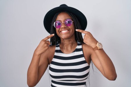 Photo for Young african american with braids wearing hat and sunglasses smiling cheerful showing and pointing with fingers teeth and mouth. dental health concept. - Royalty Free Image