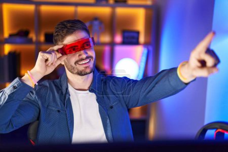 Téléchargez les photos : Jeune homme caucasien streamer jouer à un jeu vidéo en utilisant des lunettes de réalité virtuelle à la salle de jeu - en image libre de droit