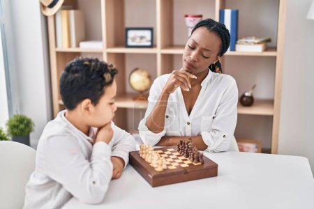 Téléchargez les photos : African American mère et fils jouant au jeu d'échecs assis sur la table à la maison - en image libre de droit