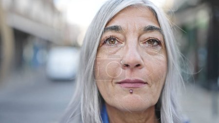 Téléchargez les photos : Femme aux cheveux gris d'âge moyen debout avec une expression sérieuse dans la rue - en image libre de droit