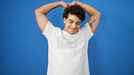 Photo for Young latin man stretching arms over isolated blue background - Royalty Free Image