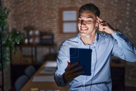 Photo for Handsome hispanic man working at the office at night smiling pointing to head with one finger, great idea or thought, good memory - Royalty Free Image
