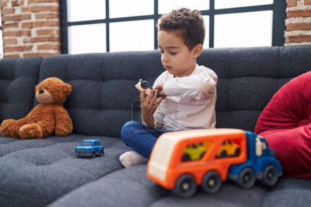 Téléchargez les photos : Adorable garçon hispanique jouant avec jouet de voiture assis sur le canapé à la maison - en image libre de droit
