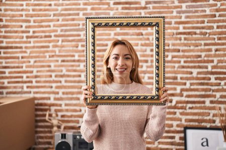 Foto de Mujer hispana sosteniendo un marco vacío sonriendo con una sonrisa alegre y fresca en la cara. mostrando dientes. - Imagen libre de derechos