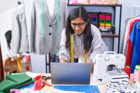 Photo for Young beautiful hispanic woman tailor smiling confident using laptop at clothing factory - Royalty Free Image