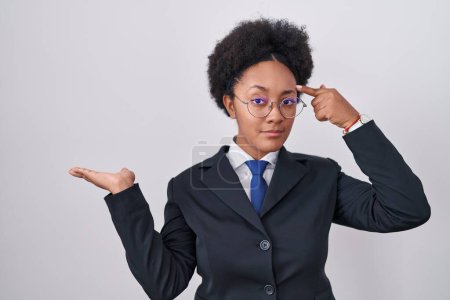Photo for Beautiful african woman with curly hair wearing business jacket and glasses confused and annoyed with open palm showing copy space and pointing finger to forehead. think about it. - Royalty Free Image