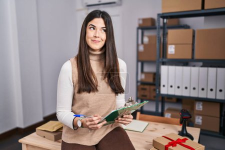 Téléchargez les photos : Jeune femme brune travaillant dans une petite entreprise e-commerce souriant regardant vers le côté et regardant loin en pensant. - en image libre de droit