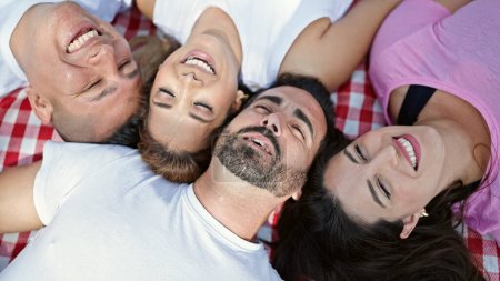 Téléchargez les photos : Groupe de personnes allongées sur une couverture de pique-nique souriant au parc - en image libre de droit