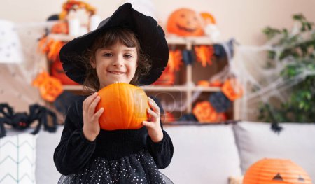 Photo for Adorable hispanic girl having halloween party holding pumpkin at home - Royalty Free Image