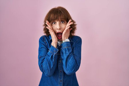 Photo for Middle age woman standing over pink background afraid and shocked, surprise and amazed expression with hands on face - Royalty Free Image