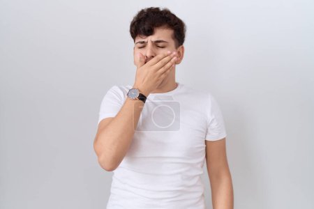Téléchargez les photos : Jeune homme non binaire portant casual t-shirt blanc ennuyé bâillement fatigué couvrant la bouche avec la main. agitation et somnolence. - en image libre de droit