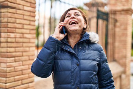 Téléchargez les photos : Femme d'âge moyen souriant confiant parler sur le smartphone à la rue - en image libre de droit