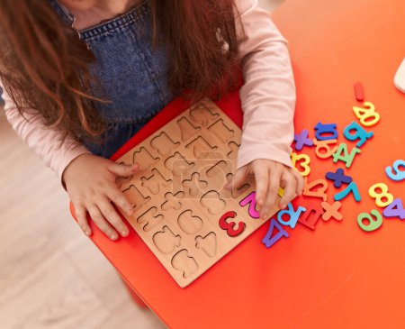 Téléchargez les photos : Adorable hispanic girl playing with maths puzzle game sitting on table at kindergarten - en image libre de droit