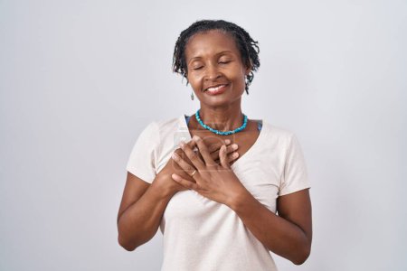 Téléchargez les photos : Femme africaine avec dreadlocks debout sur fond blanc souriant avec les mains sur la poitrine avec les yeux fermés et geste reconnaissant sur le visage. concept de santé. - en image libre de droit