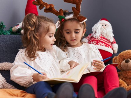 Foto de Dos niños escribiendo en el cuaderno sentado en el sofá por la decoración de Navidad en casa - Imagen libre de derechos
