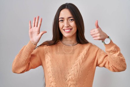 Photo for Young brunette woman standing over white background showing and pointing up with fingers number six while smiling confident and happy. - Royalty Free Image