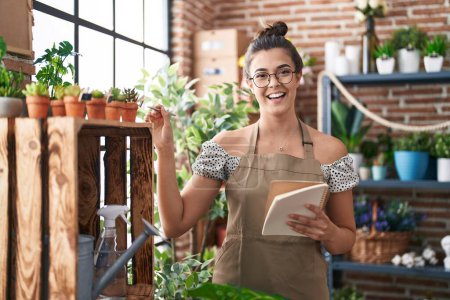 Photo for Young beautiful hispanic woman florist smiling confident reading notebook at florist - Royalty Free Image