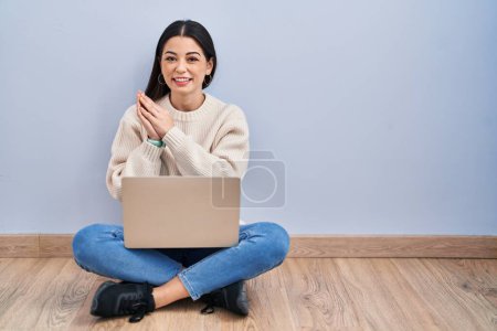 Téléchargez les photos : Jeune femme utilisant un ordinateur portable assis sur le sol à la maison applaudissements et applaudissements heureux et joyeux, souriant mains fières ensemble - en image libre de droit
