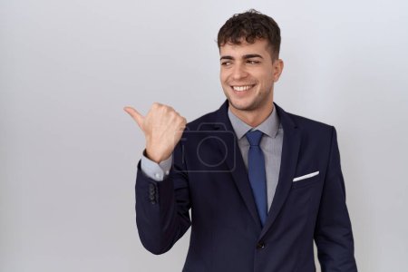 Photo for Young hispanic business man wearing suit and tie smiling with happy face looking and pointing to the side with thumb up. - Royalty Free Image