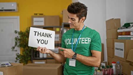 Téléchargez les photos : Jeune homme hispanique bénévole pointant pour vous remercier bannière souriant au centre de charité - en image libre de droit