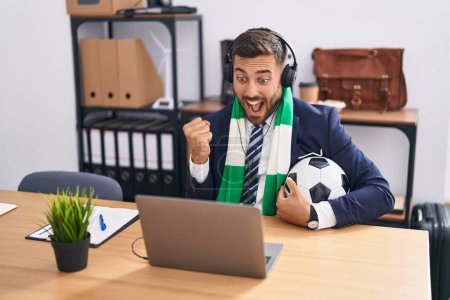 Photo for Handsome hispanic man watching football game at the office screaming proud, celebrating victory and success very excited with raised arms - Royalty Free Image