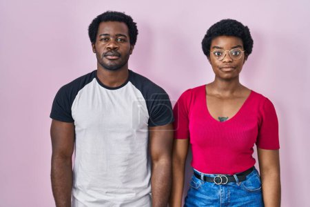 Foto de Joven pareja afroamericana de pie sobre fondo rosa relajado con expresión seria en la cara. simple y natural mirando a la cámara. - Imagen libre de derechos