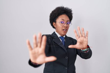 Photo for Beautiful african woman with curly hair wearing business jacket and glasses afraid and terrified with fear expression stop gesture with hands, shouting in shock. panic concept. - Royalty Free Image