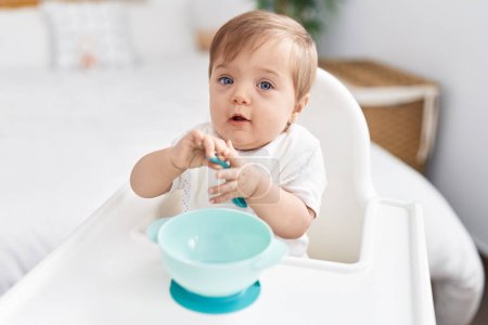 Photo for Adorable caucasian baby sitting on highchair holding spoon at bedroom - Royalty Free Image