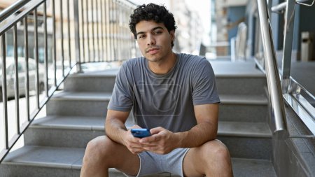 Téléchargez les photos : Young latin man using smartphone with serious expression at street - en image libre de droit