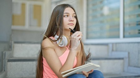 Téléchargez les photos : Jeune belle étudiante prenant des notes assis sur les escaliers en pensant à l'école - en image libre de droit