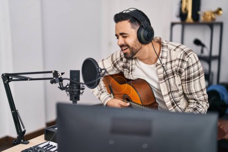 Téléchargez les photos : Jeune artiste hispanique chantant une chanson jouant de la guitare au studio de musique - en image libre de droit